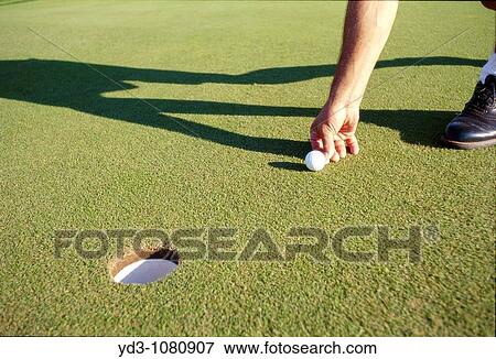 Golfer marking ball on putting green near hole with shadows View Large Photo Image Stock Photo - Golfer marking ball on putting green near hole with shadows. Fotosearch