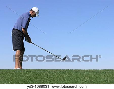 Golfer with driver setting up to hit ball off of tee, blue sky in background View Large Photo Image Stock Image - Golfer with driver setting up to hit ball off of tee, blue sky in background. Fotosearch