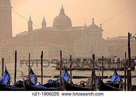 Gondolas at a dock in the Canal Grande. In front, the basilica di San Giorgio Maggiore in the isola di San Giorgio Maggiore. Venice, Veneto, Italy, Europe. View Large Photo Image Stock Photograph - Gondolas at a dock in the Canal Grande. In front, the basilica di San Giorgio Maggiore in the isola di San Giorgio Maggiore. Venice, Veneto, Italy, Europe.. Fotosearch