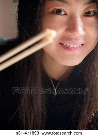 Stock Image - Good looking Chinese girl in black holding a seed of corn with chopsticks. Fotosearch