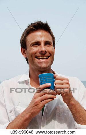 Stock Photograph - Good-looking man wearing a white shirt and holding a mug of coffee, shot in India.. Fotosearch
