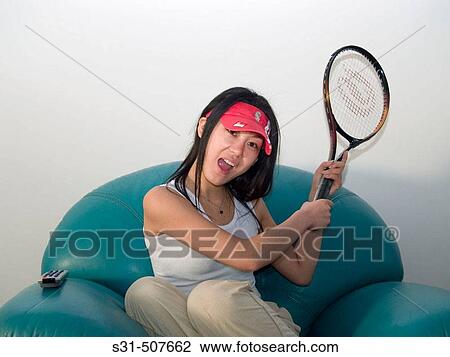 Stock Image - Good looking young asian girl watching a tennis match girl holding a racket. Fotosearch