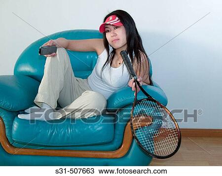 Stock Image - Good looking young asian girl watching a tennis match girl holding a racket. Fotosearch