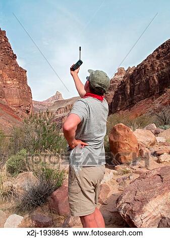Stock Photography - Grand Canyon National Park, Arizona - John West, 66, attempts to get a signal on his satellite telephone during a backpacking trip in the Grand Canyon.. Fotosearch