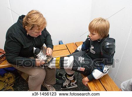 Stock Image - Grandma tightening grandsons hockey skates in locker room at indoor arena Ages 67 and 8 St Paul Minnesota MN USA. Fotosearch