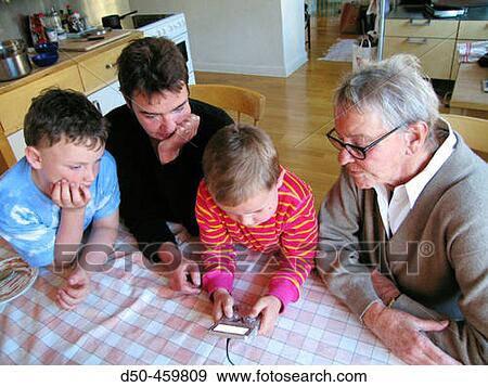 Stock Photo - Grandmother, daughter and mother of two sons, 8 and 5, look on as boy plays Gameboy game. Stockholm, Sweden. Fotosearch