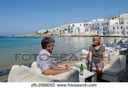 Stock Image - Greece Paros Cyclades Naousa or Naouusa relax couple with drinks near water 6.. Fotosearch