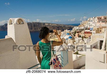 Greece Santorini Oia Cyclades white buildings and steep mountains Greek Islands beautiful peaceful place Greek with Phillipino Asian woman tourist taking pictures 11. View Large Photo Image Picture - Greece Santorini Oia Cyclades white buildings and steep mountains Greek Islands beautiful peaceful place Greek with Phillipino Asian woman tourist taking pictures 11.. Fotosearch