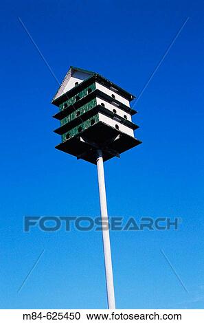 Stock Image - Green and white wooden multi-stored birdhouse on a metal pole. Fotosearch
