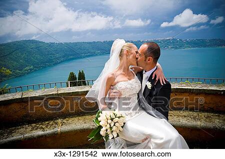 Groom holding bride and kissing in front of a Lake View Large Photo Image Stock Image - Groom holding bride and kissing in front of a Lake. Fotosearch