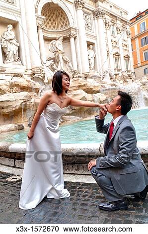 Stock Image - Groom kissing the bride's hand in Fontana di Trevi in Rome Italy. Fotosearch