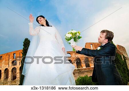 Stock Photograph - Groom offering flowers to bride at the Roman Colosseum. Fotosearch