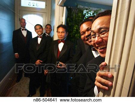 Stock Image - Groomsmen peeking around door frame. Fotosearch