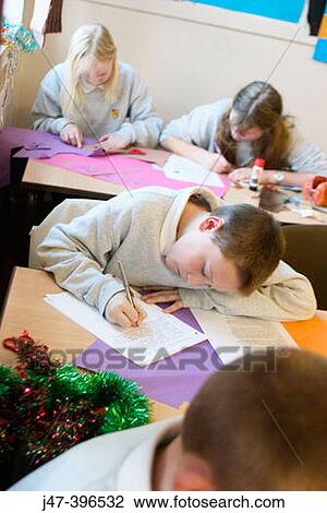 Stock Image - Group of 12 year old children, sitting in class, concentrating, drawing. Fotosearch