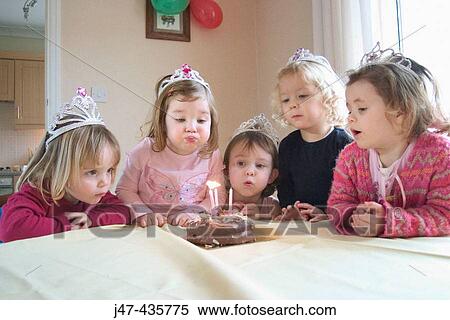 Stock Photography - Group of 3 year old girls at a party, blowing the candle out on a birthday cake. Fotosearch