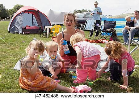 Group of children and a mum, sitting on the grass playing with bubbles, while they camp. View Large Photo Image Stock Photograph - Group of children and a mum, sitting on the grass playing with bubbles, while they camp.. Fotosearch