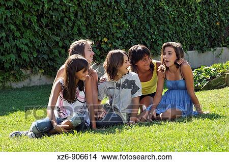 Picture - group of friends sitting on the floor of the park explaining jokes. Fotosearch