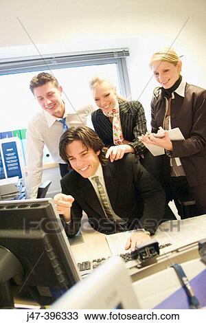 Group of young people, in an office all looking at the computer, smiling View Large Photo Image Stock Image - Group of young people, in an office all looking at the computer, smiling. Fotosearch
