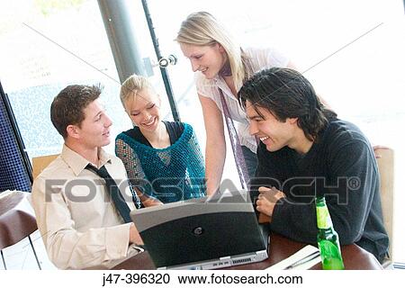 Group of young people, sitting at a table in a cafe, looking at a laptop, smiling View Large Photo Image Stock Image - Group of young people, sitting at a table in a cafe, looking at a laptop, smiling. Fotosearch