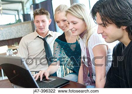 Group of young people, sitting at a table in a cafe, looking at a laptop, smiling View Large Photo Image Stock Image - Group of young people, sitting at a table in a cafe, looking at a laptop, smiling. Fotosearch