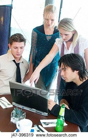 Stock Photo - Group of young people, sitting at a table in a cafe, looking at a laptop, smiling. Fotosearch