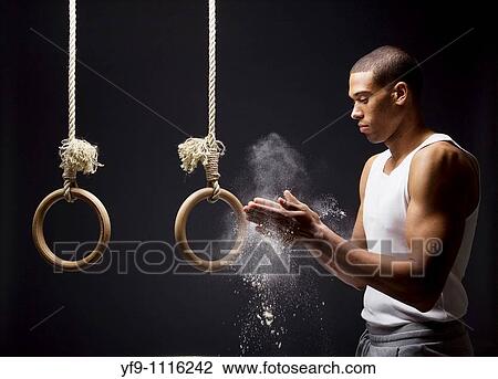 Stock Image - Gymnast man powdering hands on rings.. Fotosearch