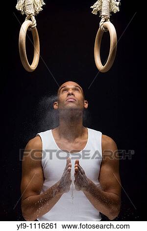 Stock Image - Gymnast man powdering hands on rings.. Fotosearch