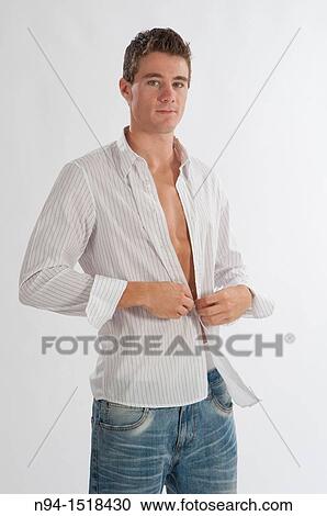Stock Image - Half-length photograph of a teenage boy putting on his white shirt.. Fotosearch