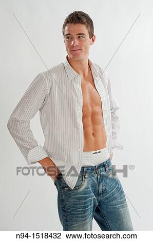 Stock Image - Half-length photograph of a teenage boy putting on his white shirt.. Fotosearch