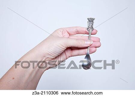 Stock Photograph - Hand Holding Little Antique Silver Spoon, Hand Gesture, Studio shot. Fotosearch
