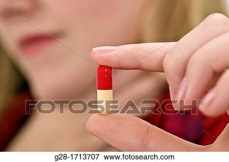 Hand of young woman blurred Holding a red and white tablet between two fingers, close up View Large Photo Image Stock Photo - Hand of young woman blurred Holding a red and white tablet between two fingers, close up. Fotosearch