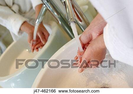 Stock Photograph - hands and their reflection under running tap at the sink. Fotosearch