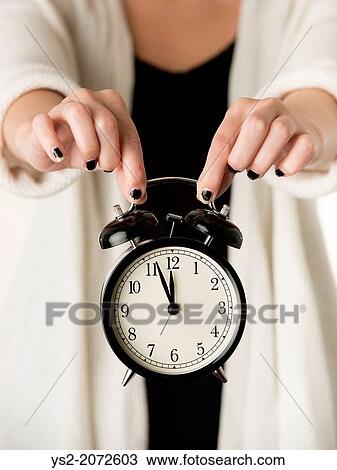 Stock Image - Hands of woman holding alarm clock.. Fotosearch