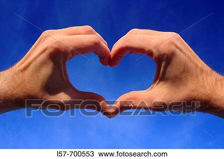 Stock Image - Hands shaping a heart in front of blue sky. Fotosearch