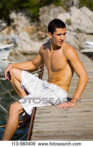 Handsome young man is sitting on a wooden wharf View Large Photo Image Stock Photo - Handsome young man is sitting on a wooden wharf. Fotosearch