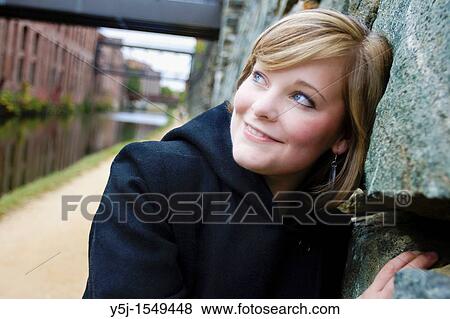 Happily smiling young Caucasian female leaning on stone wall View Large Photo Image Stock Photo - Happily smiling young Caucasian female leaning on stone wall. Fotosearch