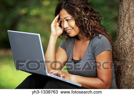 Happy African American young woman using a laptop while sitting on a grass View Large Photo Image Stock Image - Happy African American young woman using a laptop while sitting on a grass. Fotosearch