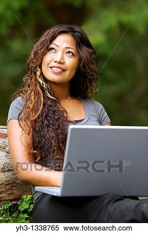 Stock Photography - Happy African American young woman using a laptop while sitting on a grass. Fotosearch