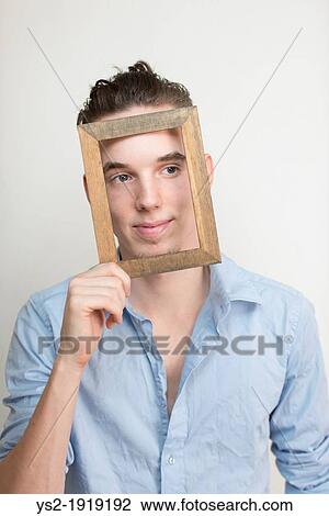 Happy and carefree young adult man posing with wooden frame in front of his face View Large Photo Image Stock Image - Happy and carefree young adult man posing with wooden frame in front of his face. Fotosearch
