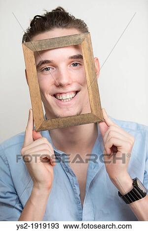 Happy and carefree young adult man posing with wooden frame in front of his face View Large Photo Image Stock Image - Happy and carefree young adult man posing with wooden frame in front of his face. Fotosearch