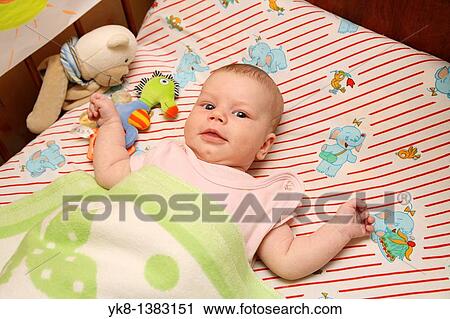 Stock Image - Happy Baby Infant Lying in Bed with Toy. Fotosearch