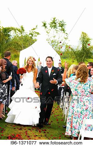 happy bride and groom exiting their wedding ceremony hand in hand as guests throw red rose petals in the air View Large Photo Image Stock Photo - happy bride and groom exiting their wedding ceremony hand in hand as guests throw red rose petals in the air. Fotosearch