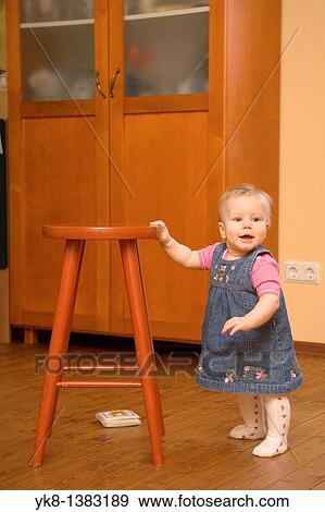 Happy Eight Month Old Infant Girl Standing by Stool Chair View Large Photo Image Stock Photo - Happy Eight Month Old Infant Girl Standing by Stool Chair. Fotosearch