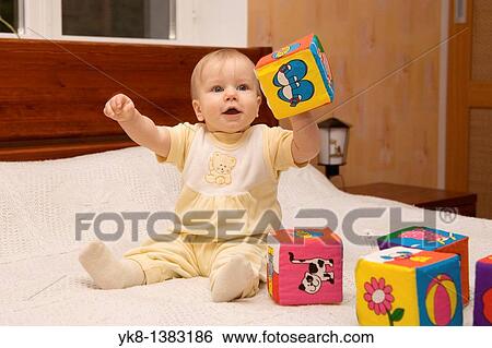 Stock Photograph - Happy Eight Month Old Infant Girl Playing With Cubes on Bed. Fotosearch