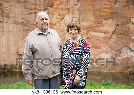 Stock Photograph - Happy Elderly Senior Couple Standing by Valgemetsa Sandstone Outcrop. Fotosearch