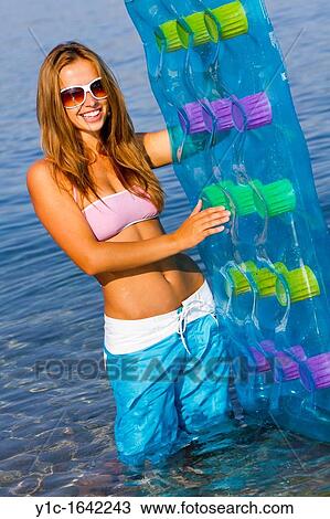 Stock Image - Happy girl in the water with inflatable mattress in hand. Fotosearch
