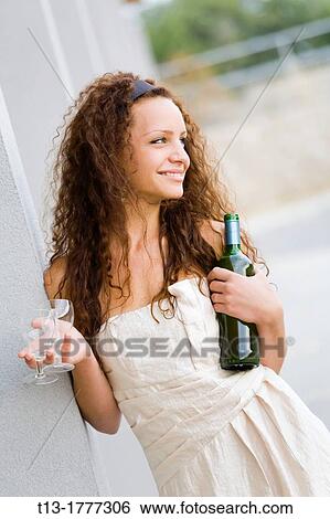 Stock Photograph - Happy girl wiht a bottle and glasses in hands expecting someone. Fotosearch