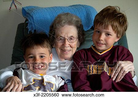 Stock Image - Happy Great grandmother age 95 holding her two great grandsons age 7 and 10 in her home. Battle Lake Minnesota MN USA.. Fotosearch