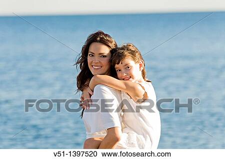 Happy mother carrying her daughter at the beach and looking at camera View Large Photo Image Stock Image - Happy mother carrying her daughter at the beach and looking at camera. Fotosearch