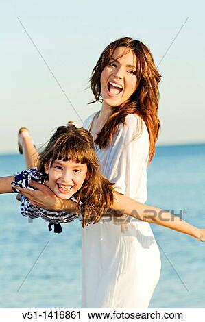 Happy mother playing with her daughter at the beach and smiling at camera View Large Photo Image Stock Image - Happy mother playing with her daughter at the beach and smiling at camera. Fotosearch